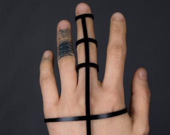 Könnte beinhalten: Eine Hand trägt ein schwarzes Lederarmband und einen schwarzen Lederring am Mittelfinger. Der Ring besteht aus mehreren Bändern, die ein geometrisches Muster bilden.