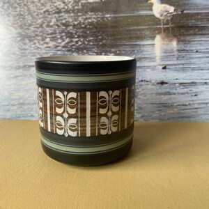 Peut inclure: Une tasse cylindrique en céramique avec un extérieur noir, présentant un motif géométrique marron et blanc. La tasse a une bande vert clair et un intérieur blanc. La tasse est probablement utilisée pour boire des boissons.