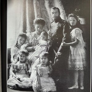May include: Black and white photograph of a family portrait. A man in a military uniform stands with a woman holding a baby. Several children in dresses are also in the image. The text at the bottom reads, "The family of Emperor Nicholas II."