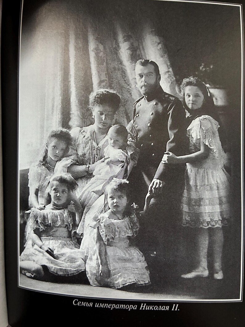 May include: Black and white photograph of a family portrait. A man in a military uniform stands with a woman holding a baby. Several children in dresses are also in the image. The text at the bottom reads, "The family of Emperor Nicholas II."