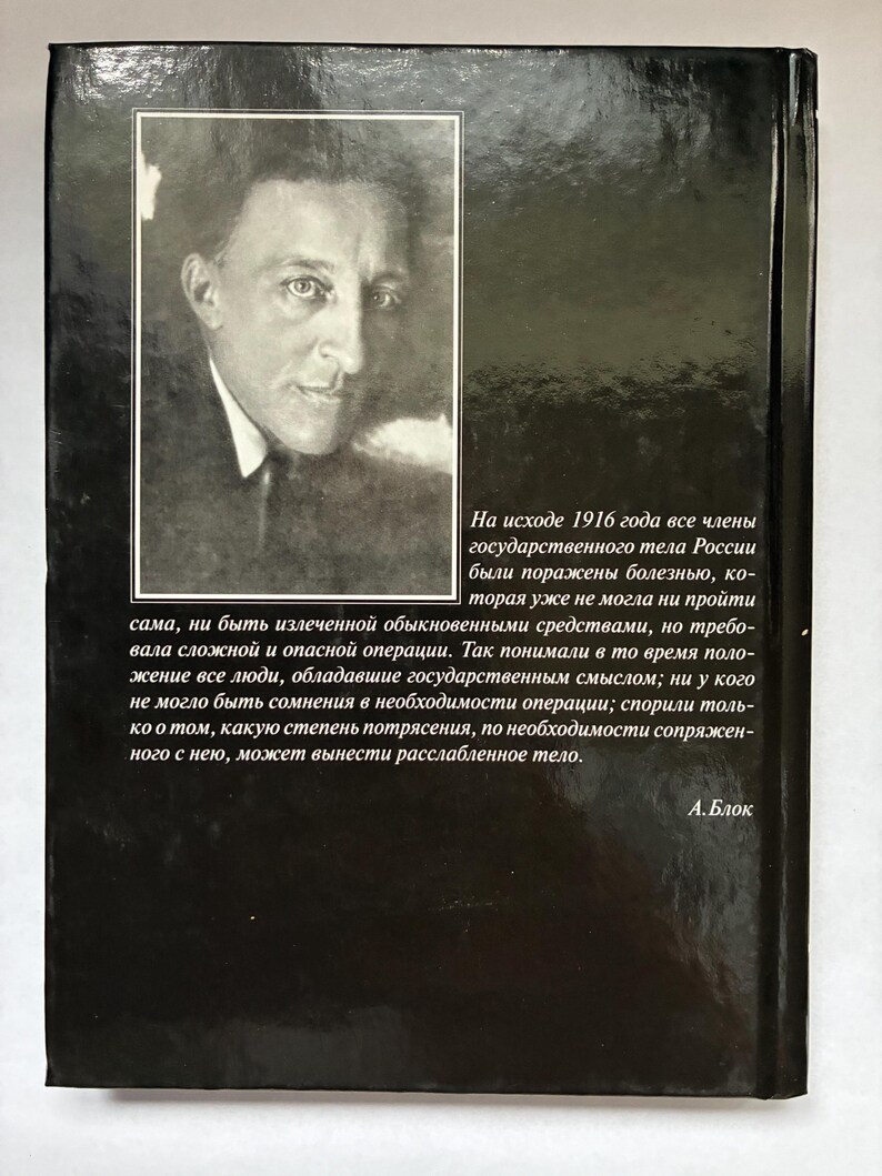 May include: A black book cover featuring a portrait of a man in a suit and tie. The book has text in Russian on the back cover, with the author's name, A. Blok, at the bottom. The cover is glossy and reflects light.