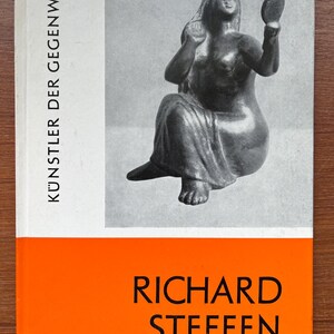 Puede incluir: Portada de libro con una imagen en blanco y negro de una estatua sentada sosteniendo un espejo. El título es "KÜNSTLER DER GEGENWART" y el nombre del autor, "RICHARD STEFFEN", está en blanco sobre un fondo naranja.