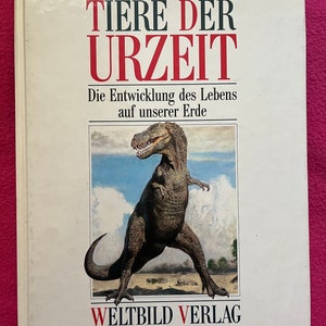 Pode incluir: Um livro intitulado "TIERE DER URZEIT" com uma ilustração de dinossauro. O título é em vermelho e preto, com o subtítulo "Die Entwicklung des Lebens auf unserer Erde." O nome da editora, WELTBILD VERLAG, está na parte inferior.