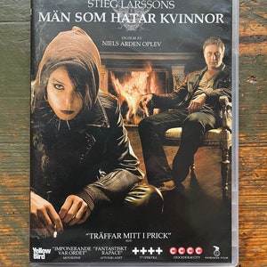Könnte beinhalten: DVD-Hülle für den Film "Verblendung" mit Michael Nyqvist und Noomi Rapace. Das Cover zeigt zwei Personen vor einem Kamin. Der Titel ist auf Schwedisch.