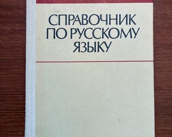 Puede incluir: Un libro de tapa dura con una cubierta color crema y un lomo burdeos. El título, en ruso, dice "Manual de la lengua rusa". Los nombres de los autores están impresos encima del título. El libro está sobre una superficie de madera.