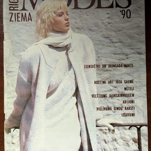 Puede incluir: Una portada de revista vintage con una mujer vestida con un atuendo color crema. El título de la revista "MODES" se muestra en letras grandes y oscuras, con "ZIEMA" y "'90" también visibles. La portada incluye texto en letón.
