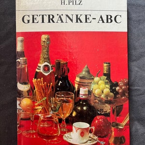 Puede incluir: Una portada de libro vintage titulada "GETRÄNKE-ABC" de H. Pilz, con un fondo rojo vibrante. La portada muestra una variedad de bebidas, incluyendo champán, vino y cócteles, con copas y botellas.