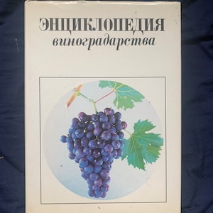 Puede incluir: Libro de tapa dura con el título "Энциклопедия виноградарства" en texto negro. La portada presenta un racimo de uvas moradas con hojas verdes sobre fondo blanco.