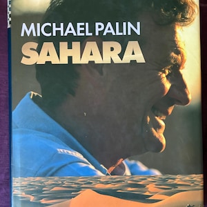 Puede incluir: Portada del libro "Sahara" de Michael Palin. La imagen muestra un retrato de Palin con un paisaje desértico. El texto "As seen on BBC" también es visible.