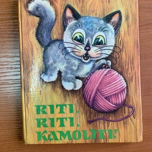May include: A vintage children's book cover featuring a gray kitten with a pink ball of yarn. The kitten has large green eyes and is set against a wood-grain background. The title "RITI RITI KAMOLITI!" is printed in green.