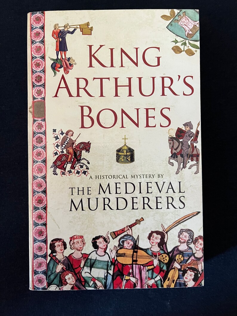 May include: A book titled "King Arthur's Bones" by The Medieval Murderers. The cover displays medieval illustrations of figures, musicians, and decorative borders with floral patterns. The book is a historical mystery, with text in red and black.