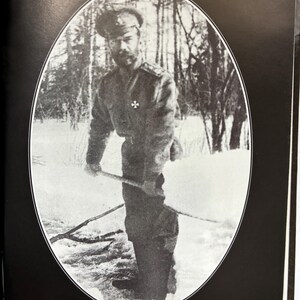May include: Black and white photograph of a man in military attire, holding a stick, standing in a snowy outdoor setting. The image is framed in an oval shape. Text at the bottom reads "Nikolai II under house arrest."