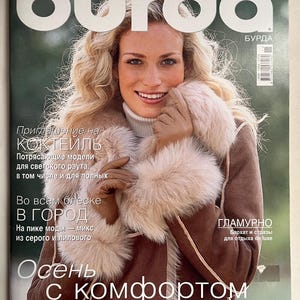 Op de afbeelding: Een tijdschriftomslag met een lachende vrouw met blond haar die een bruine jas met een bontkraag draagt. De tijdschrifttitel "burda" is te zien, met tekst in het Russisch. De cover suggereert een modethema.