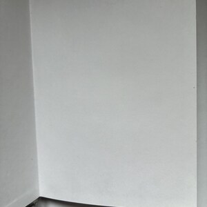 May include: Open book with blank white pages. The book is open to a double-page spread, with the pages appearing clean and unused. The binding is visible on the left side, with a black spine. The pages are smooth and the lighting is soft.