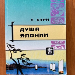 Puede incluir: Un libro antiguo titulado "El alma de Japón" en ruso. La portada presenta un fondo turquesa y amarillo con ilustraciones y texto de estilo japonés. El título del libro se muestra en negrita, en letras negras.