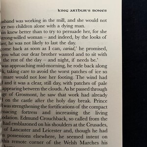 May include: An open book with text from "King Arthur's Bones" is shown. The text is in black font on a white page. The title "KING ARTHUR'S BONES" is at the top. The book is on a dark surface.