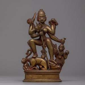 May include: A gold-coloured metal sculpture of a Hindu deity standing on a beast with a smaller figure at her side. The deity holds a trident in one hand and a weapon in the other.