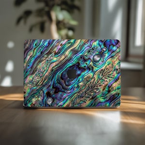 May include: A laptop case with an iridescent abalone shell design. The case features a swirling pattern of blues, greens, purples, and hints of gold. The Apple logo is visible on the case.