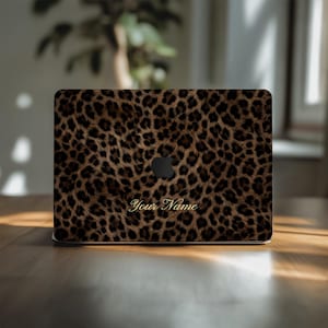 May include: A laptop with a leopard print design. The cover features a brown and black spotted pattern, with the Apple logo in black. The words "Your Name" are written in gold script.