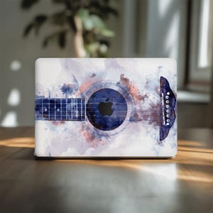 May include: A white laptop skin featuring a watercolor design of an acoustic guitar. The design incorporates shades of blue, purple, and brown, with a black Apple logo in the center. The guitar's strings and soundhole are clearly visible.