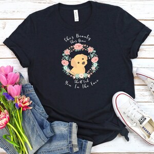 Puede incluir: Una camiseta negra con una corona de flores y un cachorro golden retriever. El texto en la camiseta dice "She's Beauty She's Grace She'll Rub You In The Face".