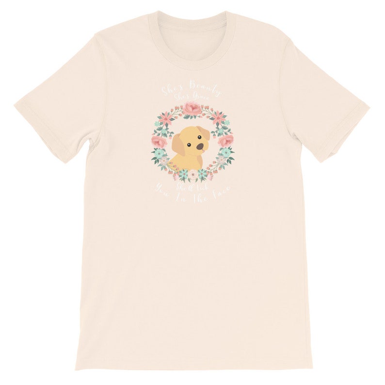 Puede incluir: Una camiseta beige con una corona de flores y un perro amarillo en el centro. El texto "She's really the queen of the whole town" est&aacute; escrito en blanco.