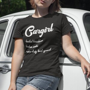 May include: Two women wearing black and white t-shirts with the text "Cargirl" and a definition of the word. The text on the shirts reads "busted knuckles, broken nails, makes every look good".