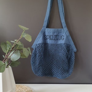 May include: A blue canvas tote bag with a mesh bottom. The bag has a black embroidered word "SPIELZEUG" on the front.