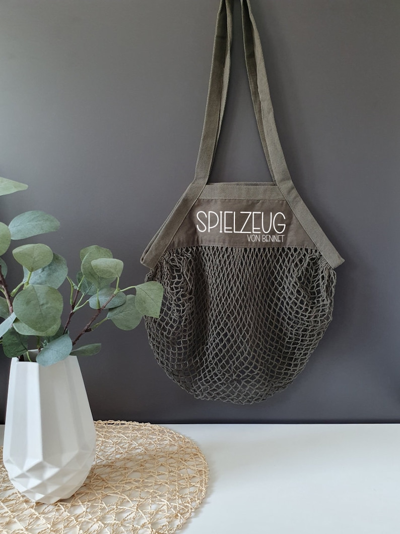 May include: A green canvas tote bag with a mesh bottom. The bag has a white embroidered label that says "Spielzeug von Bennet".