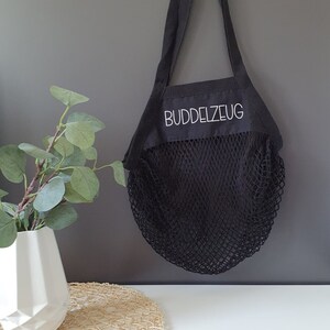 May include: Black reusable mesh shopping bag with a black fabric top and white text that reads "BUDDELZEUG".