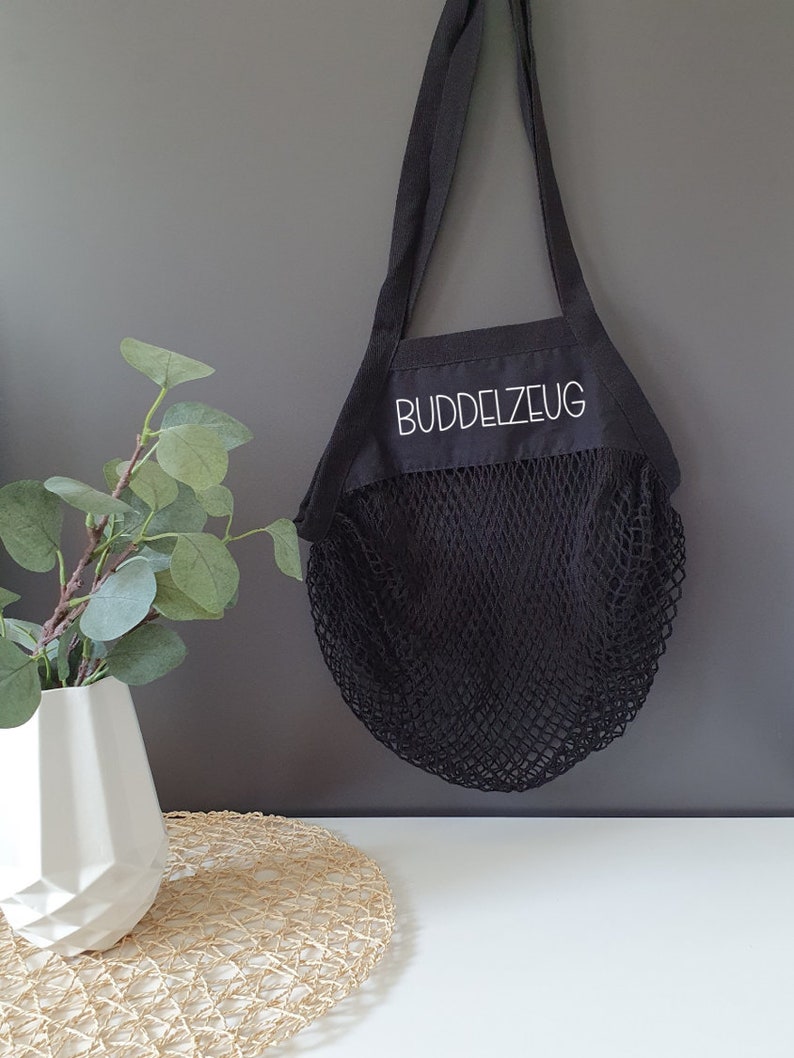 May include: Black reusable mesh shopping bag with a black fabric top and white text that reads "BUDDELZEUG".