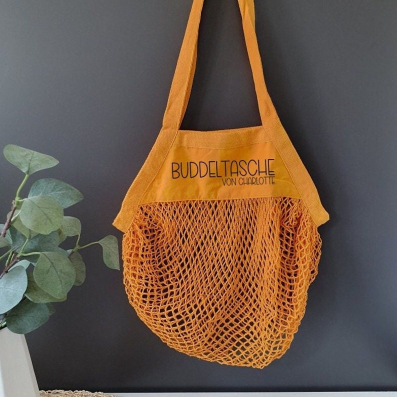 Sonnengelbe Netztasche mit der Beschriftung Buddeltasche von Charlotte in schwarzer Farbe.