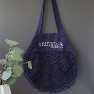 May include: A navy blue mesh shopping bag with a dark blue canvas top. The canvas top has the text "Buddeltasche von Charlotte" embroidered in white.