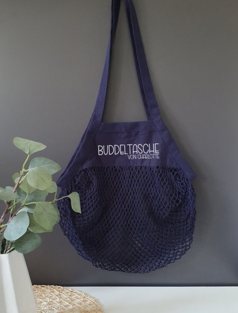 May include: A navy blue mesh shopping bag with a dark blue canvas top. The canvas top has the text "Buddeltasche von Charlotte" embroidered in white.