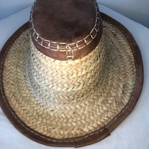 May include: A wide-brimmed straw hat with a brown leather band and crown. The hat is woven with a herringbone pattern.