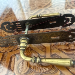 May include: Antique brass door handle with intricate floral designs and a keyhole. The handle has a curved lever and a decorative backplate.