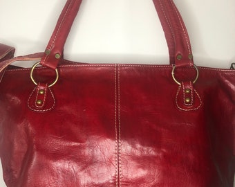 May include: A red leather tote bag with two top handles and a white stitch detail. The bag has two gold metal rings on the front.