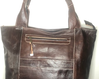 Puede incluir: Un bolso tote de cuero marrón con un bolsillo con cremallera y costuras blancas. El bolso tiene dos asas superiores.