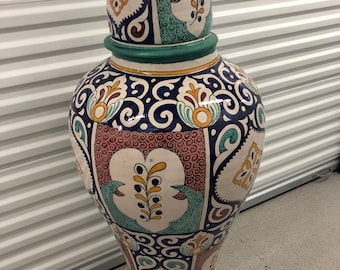 May include: A large, white ceramic vase with a green lid. The vase is decorated with intricate blue, red, yellow, and green floral patterns.