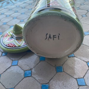 May include: A green and white ceramic jar with a geometric pattern. The bottom of the jar is white and has the word "SAFI" written in black.