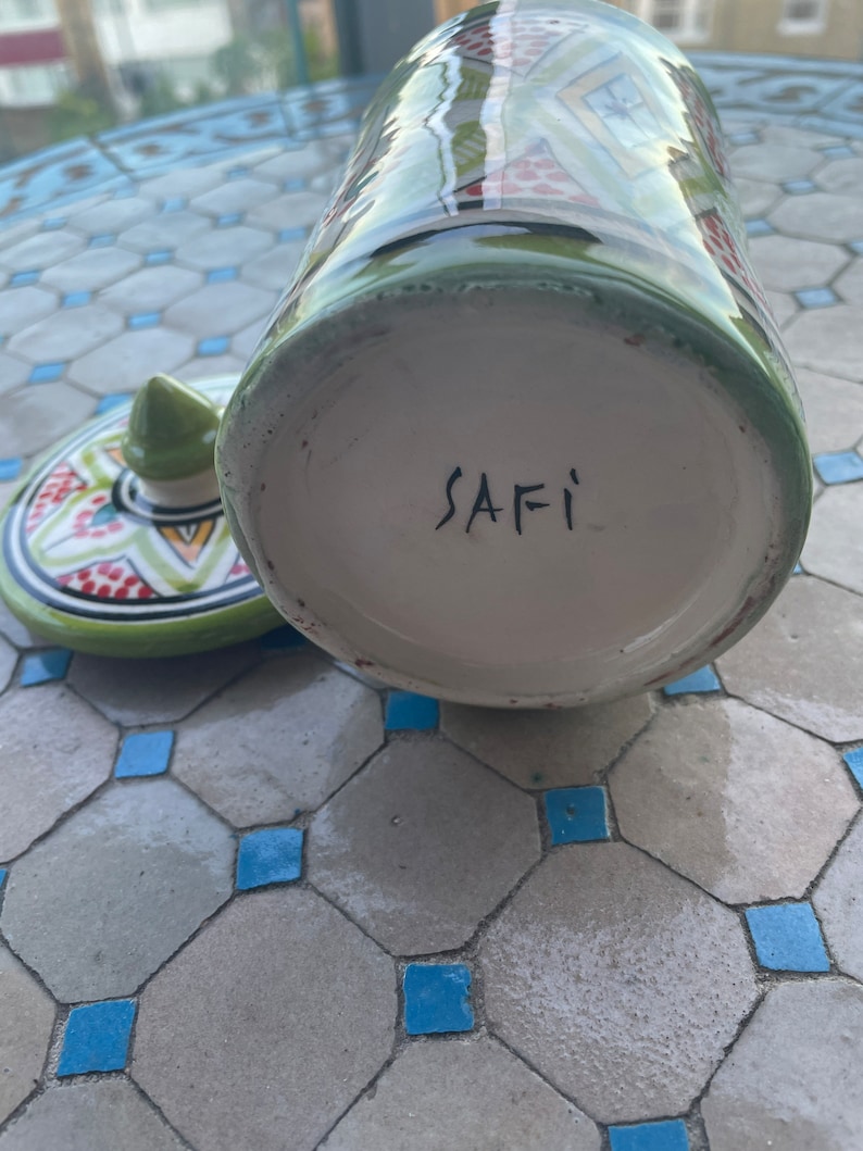 May include: A green and white ceramic jar with a geometric pattern. The bottom of the jar is white and has the word "SAFI" written in black.