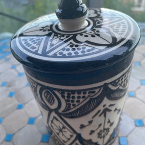 May include: A white ceramic jar with a black and white geometric design. The jar has a lid with a pointed top and a black and white geometric design.