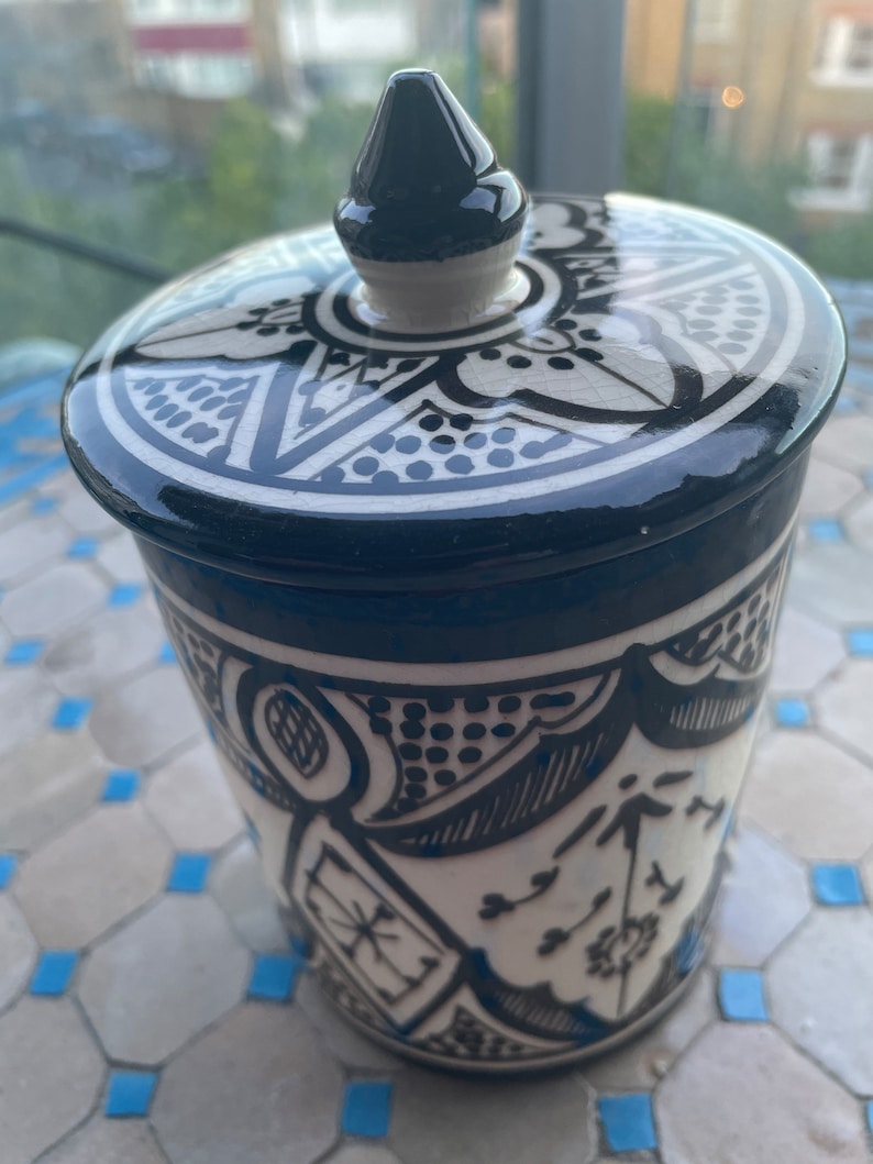 May include: A white ceramic jar with a black and white geometric design. The jar has a lid with a pointed top and a black and white geometric design.