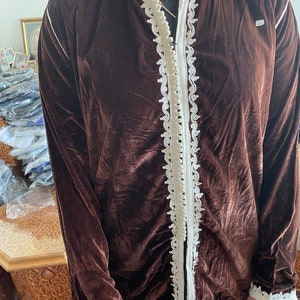May include: A brown velvet jacket with white embroidered trim around the collar, cuffs, and front opening. The jacket has a zip closure.