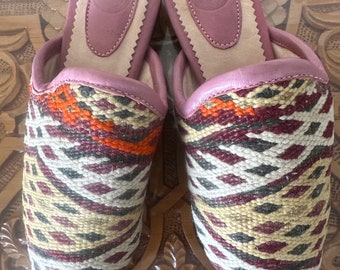 May include: A pair of pointed-toe slippers with a geometric pattern in shades of brown, beige, white, and orange. The slippers have a pink leather lining and a leather insole.