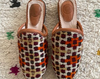 May include: A pair of brown leather slippers with a colorful geometric pattern. The slippers have a pointed toe and a flat sole.