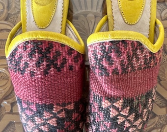 May include: A pair of pink and black patterned slippers with yellow leather trim and a white leather insole. The insoles have the letters "IA" stamped on them.