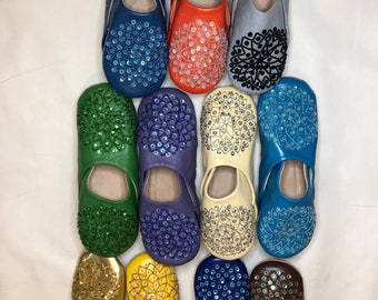 Puede incluir: Una colección de 10 pares de zapatillas de cuero de colores con intrincados diseños de cuentas. Las zapatillas están dispuestas en una pila, con los dedos apuntando hacia arriba. Las zapatillas son de diferentes colores, incluyendo azul, verde, rojo, naranja, amarillo y marrón.