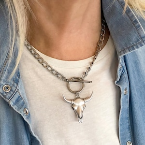 May include: A silver chain necklace with a silver bull skull pendant. The chain has a toggle clasp.