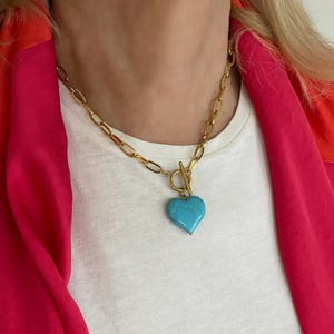 Peut inclure: Collier chaîne doré avec un pendentif en forme de cœur turquoise. Le collier est doté d'un fermoir à bascule et d'une chaîne à maillons épais. Le pendentif en forme de cœur est d'une teinte turquoise vibrante.
